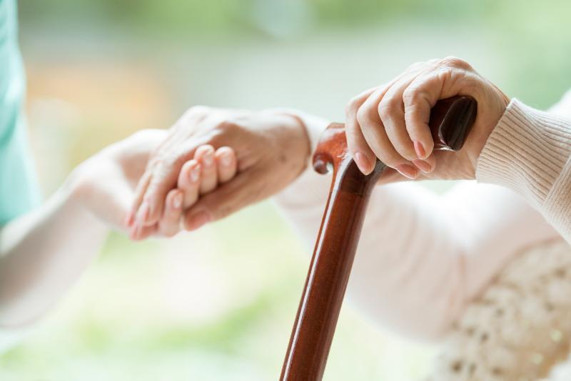 杖を持った高齢者の手を握る若者の手
