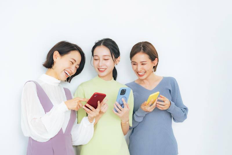 スマートフォンを手に笑顔で会話する女性３人