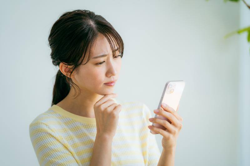 スマートフォンを片手に悩む女性