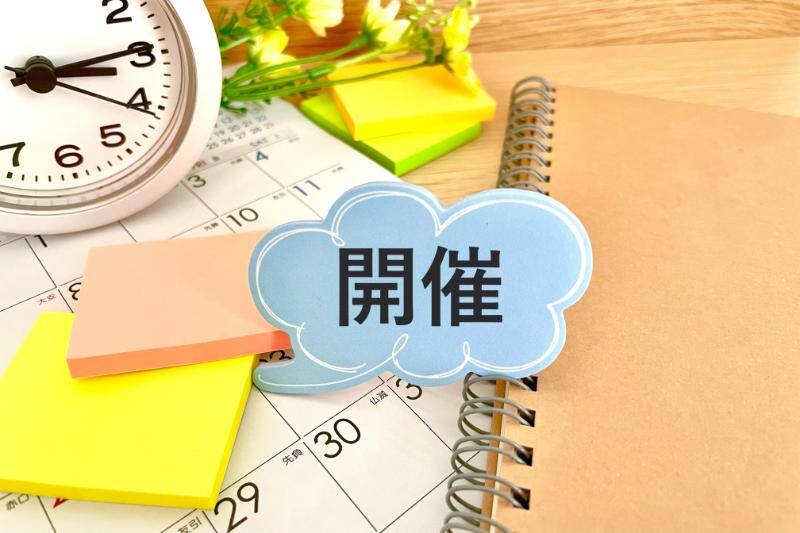 卓上に置かれたカレンダーやノート付箋に囲まれた「開催」と書かれた青い吹き出し
