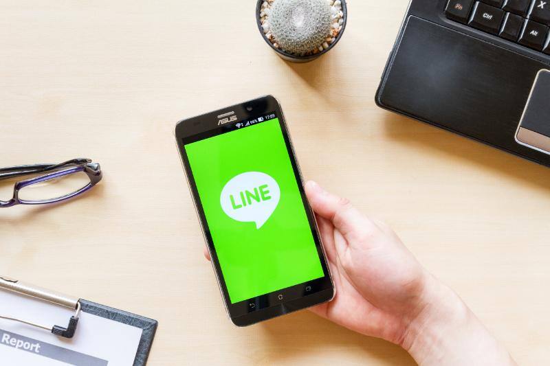 デスク上でLINE画面を表示したスマートフォンを持つ手