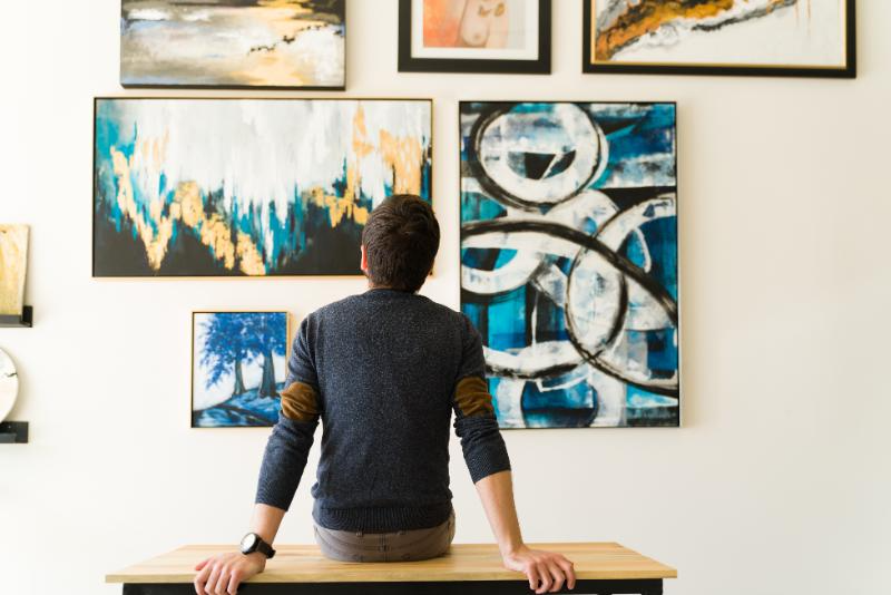 ベンチに腰掛けて絵画を眺める後ろ姿の男性